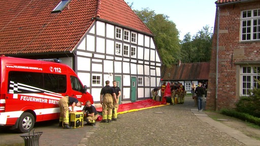 Es ist ein Feuerwehrauto und Feuerwehrmänner auf einem Bauernhof zu sehen, welche den Einsatz bei Katastrophen üben.