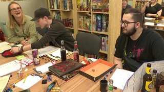 Eine kleine Runde von menschen sitzt am Tisch und spielt gemeinsam Dungeons and Dragons. 