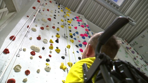 Ein Rollstuhlfahrer vor einer Kletterwand