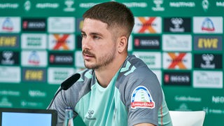 Werder-Spieler Romano Schmid sitzt vor einer Werbewand und hinter einem Mikrofon