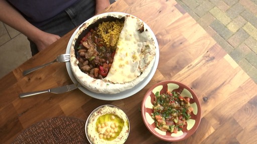 Lammfleisch und Reis in einem Brotmantel, daneben zwei Schalen mit Hummus und Baba Ganousch