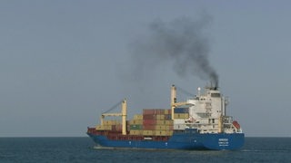 Schiff fährt auf dem Meer und ist am qualmen. Es sind Container geladen.