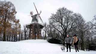 Spaziergänger laufen durch den Schnee an der Mühle am Wall vorbei. 