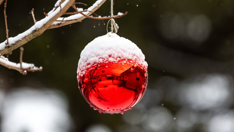 Schnee liegt auf einer Christbaumkugel.