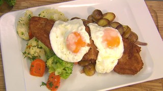 Schnitzel mit Gemüse, Bratkartoffeln und Spiegeleier, auf einem Teller angerichtet