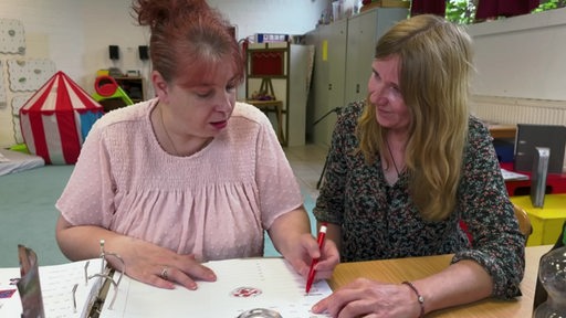 Während eines Workshops zum Lesen und Schreiben lernen sitzen zwei Frauen an einem Tisch