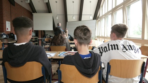 Schüler sitzen in einem Klassenzimmer vor einer weißen Tafel