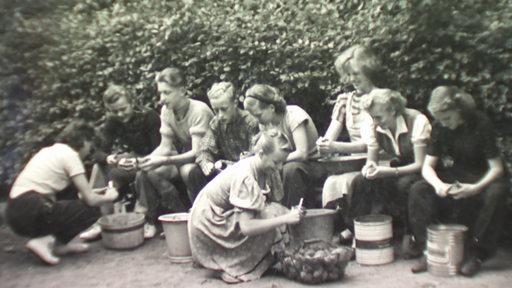 Mehrere Schülerinnen und Schüler schälen in Kartoffeln im Unterricht an einer Schule in der Nachkriegszeit.