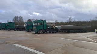 Mehrere Lkw mit großen Bauteilen stehen auf einem Parkplatz.