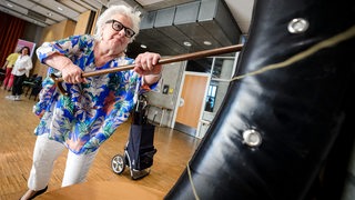 Eine Seniorin mit Krückstock schlägt während eines Selbstverteidigungskurses ("Cane Fu") mit ihrem Stock auf ein Polster 