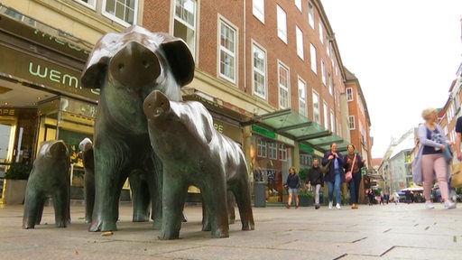 Die Sögestraße in der Bremer Innenstadt. Zu sehen sind im Vordergrund die Skulpturen der Schweine und nach hinten hin die Geschäfte der Sögestraße mit Passanten.