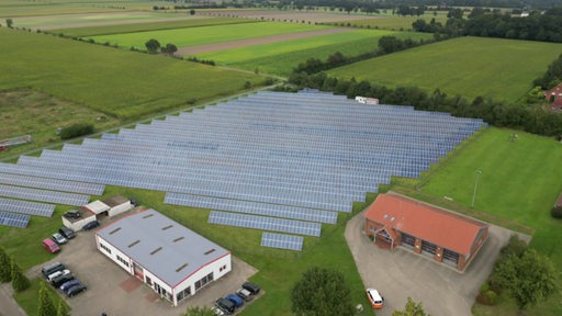 Auf einem Feld steht neben einigen Gebäuden eine größere Photovoltaikanlage