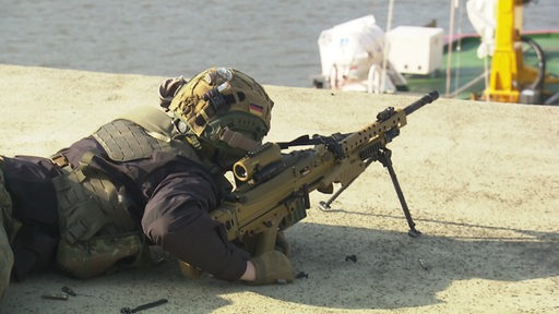 Ein Soldat liegt in voller Montur auf dem Boden und schaut durch das Visier seiner vollautomatischen Waffe.