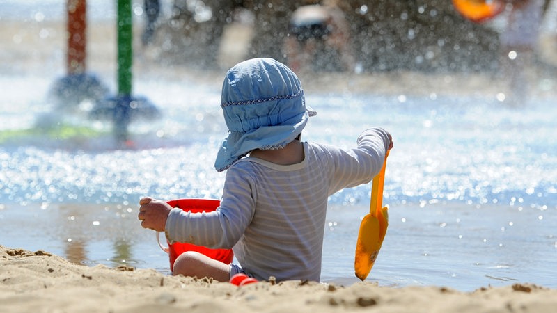 Ein kleiner Junge mit Sonnenmütze spielt bei schönstem Sommerwetter am Weserstrand von Bremerhaven (Bremen). 