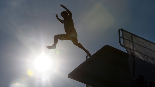 Ein junger Mann springt von einem Sprungturm ins Becken.