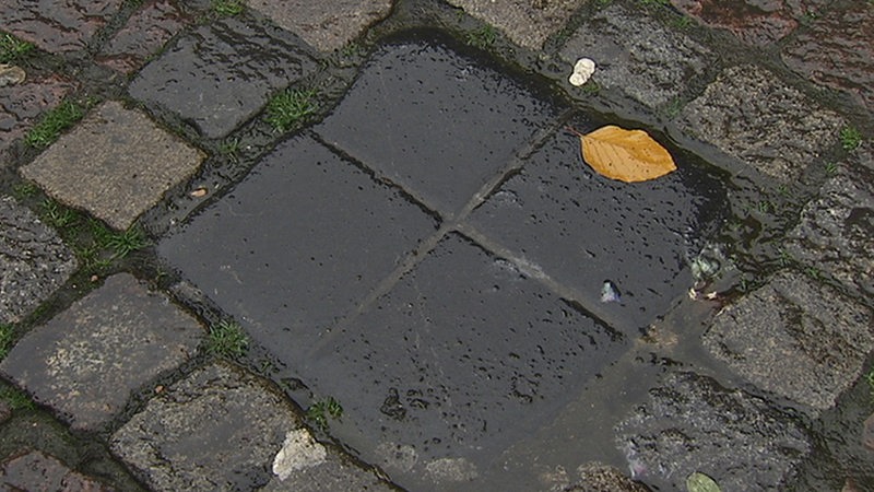 Ein Stein mit einem Kreuz darauf im Straßenpflaster.