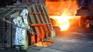 Ein Mitarbeiter in Schutzkleidung überwacht die Temperatur von Roheisen beim Abstich an einem Hochofen der ArcelorMittal Eisenhüttenstadt GmbH.