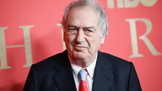 Der Regisseur Stephen Frears steht vor einer roten Wand und schaut in eine Kamera.