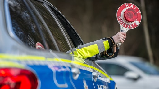 Eine Hand hält eine Polizeikelle mit der Aufschrift "Halt-Polizei" aus dem Fenster.