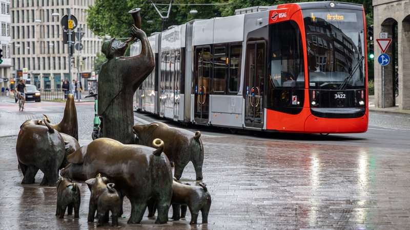 Eine Straßenbahn fährt bei leichtem Regen an der Skulpturengruppe des Schweinehirten am Anfang der Sögestraße in der Bremer Innenstadt vorbei. 