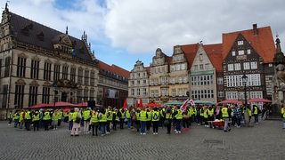 Beschäftigte im Einzelhandel stehen mit Verdi-Warnwesten auf dem Bremer Marktplatz