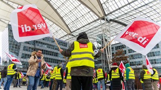 Verdi Streik am Flughafen. Mitglieder schwenken vor einem Flughafen ver.di-Flaggen.