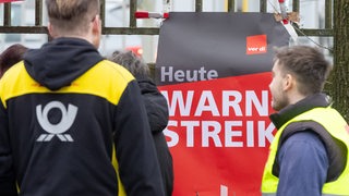 Auf einem Plakat steht "Heute Warnstreik". Davor stehen ein Mann in Briefzusteller-Kleidung und einer in Warnweste.