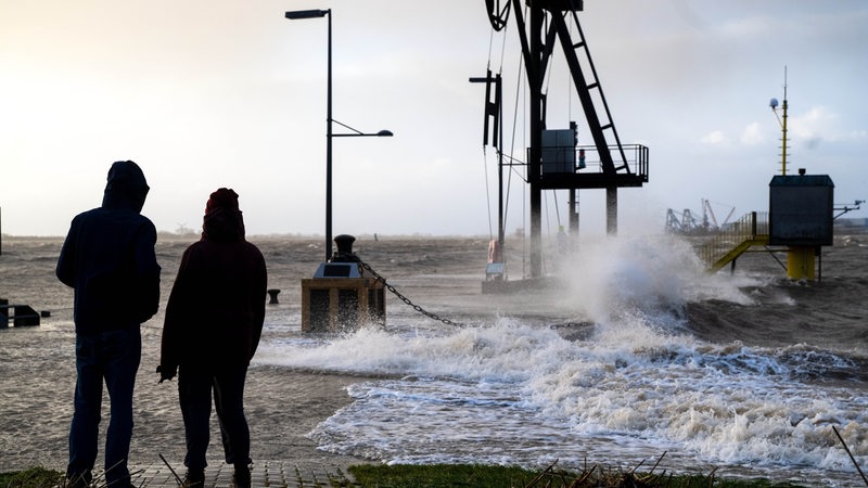 Spaziergänger laufen bei Sturmflut am Ufer der Wesermündung in Bremerhaven entlang.