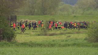 Menschen in Feuerwehruniform laufen in einer Kette durch eine Wiese