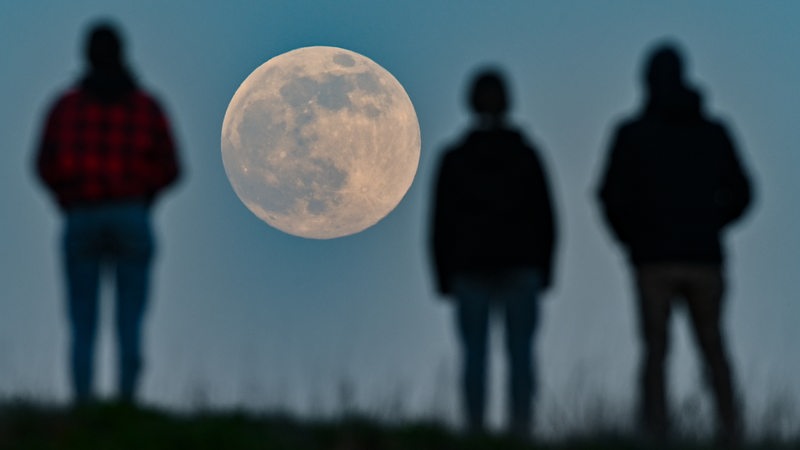 Menschen stehen auf einem Hügel und beobachten den aufgehenden Mond. 