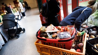 Eine Frau sammelt bei der Tafel Obst aus einer Kiste während andere an der Lebensmittelausgabe stehen