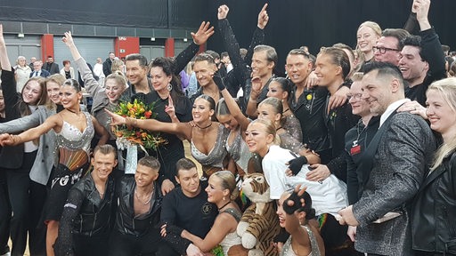 Die Tänzerinnen und Tänzer des Grün-Gold-Clubs mit Trainer Roberto Albanese jubeln beim Gruppenfoto nach dem Bundesligasieg.