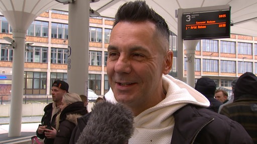 Grün-Gold-Trainer Roberto Albanese steht lächelnd am Bremer Busbahnhof beim Interview vor der Abfahrt nach Ludwigsburg zur Tanz-Meisterschaft.