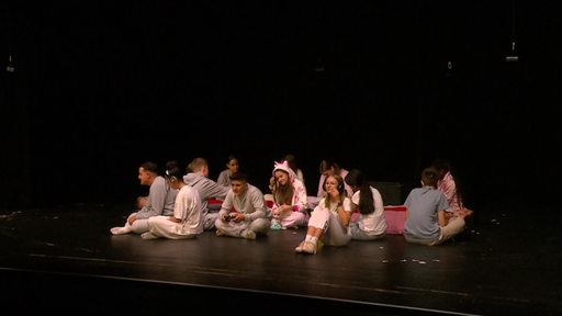 Schüler der Gesamtschule Bremen-Ost sitzen auf einer Theaterbühne.