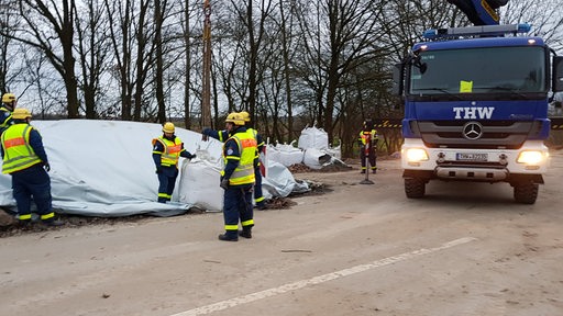 THW-Helfer stehen vor einem Sandhaufen auf einer Straße