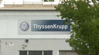 Auf einer weißen Industriehalle steht das Logo und der Schriftzug des Unternehm ThyssenKrupp.