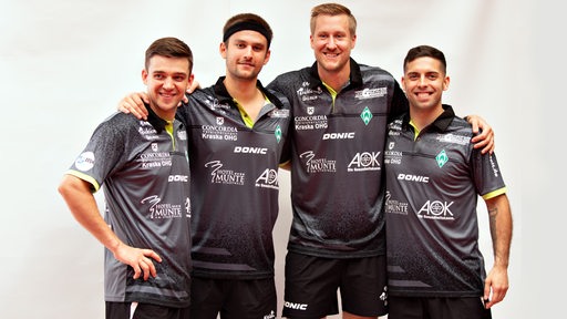 Die vier Tischtennisspieler von Werder Bremen Mattias Falck, Kirill Gerassimenko, Marcelo Aguirre und Cristian Pletea posieren lächelnd Arm in Arm für ein Teamfoto.