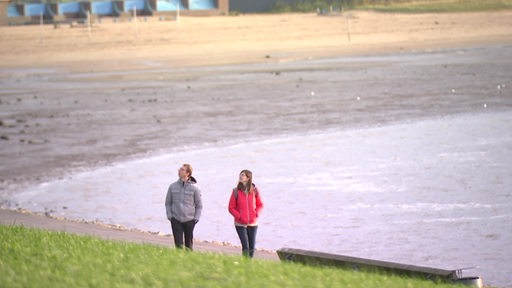 Zwei Personen während eines Spaziergangs am Deich, im Hintergrund das Meer