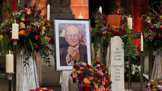 Blumengestecke stehen vor einem Bild von Willi Lemke im Bremer Dom