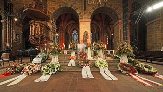 Blumengestecke, Kränze und Kerzen stehen vor einem Bild von Willi Lemke im Bremer Dom