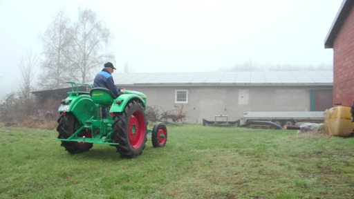 Ein Landwirt fährt auf seinem Trecker über den Rasen auf seinem Hof. 