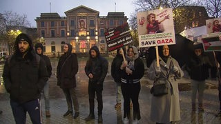 Einige Menschen halten während einer Demonstration vor dem Überseemuseum Schilder hoch.