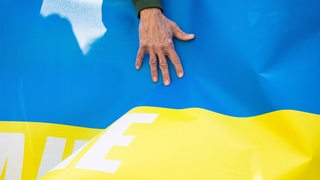 Eine Männerhand ist auf einem Transparent, das die Farben blau und gelb der ukrainischen Nationalflagge hat, zu sehen.