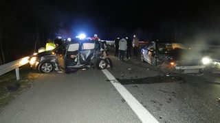 Ein stark beschädigtes Auto steht quer zu einer Fahrbahn, dahinter Blaulicht