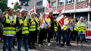 Menschen mit gelben Warnwesten und Fahnen mit der Aufschrift "Verdi" stehen in einer Fußgängerzone.