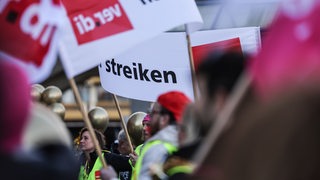 Menschen in Warnwesten und mit Verdi-Fahnen streiken