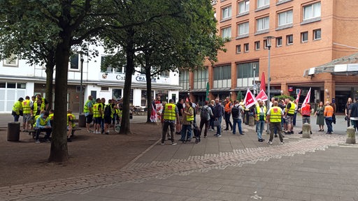 Menschen in gelben Warnwesten stehen vor einem Gebäude.