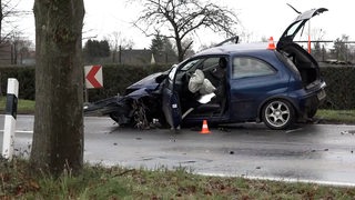 Ein völlig zerstörtes Auto steht auf einer Landstraße.