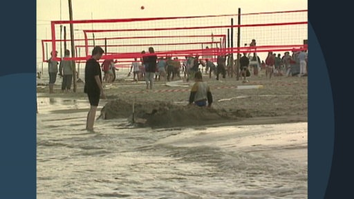 Auf einem Strand spielen Menschen zwischen gespannten Volleyballnetzen, im vordergrund das Meer.