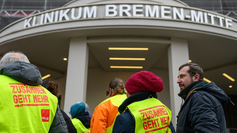 Teilnehmer des Warnstreiks stehen vor dem Klinikum Bremen-Mitte. Sie tragen Warnwesten mit der Aufschrift "Zusammen geht mehr".